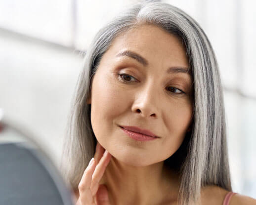 Woman looking at mirror after applying Luminous skincare product